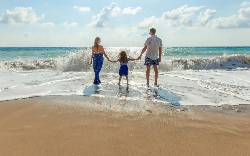 Eine Familie hält sich am Strand an den Händen und blickt aufs Meer